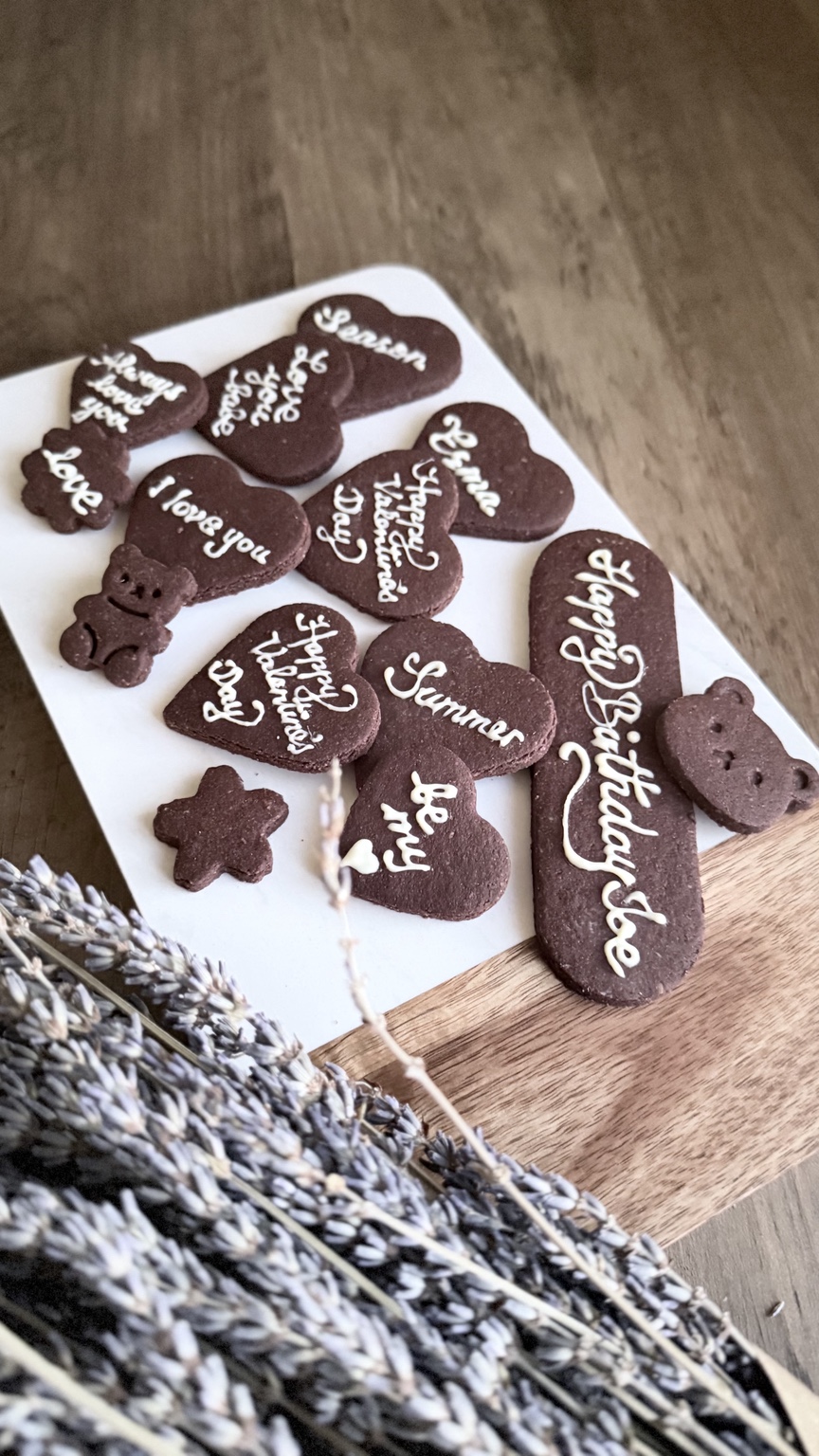 Crémia chocolate cookie plaques with handwritten wishes, arranged on a wooden table beside dried flowers